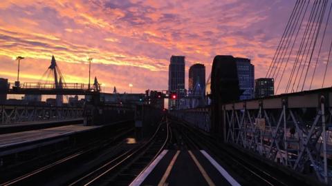 Charing Cross station at sunset. The picture looks out onto the tracks with some of the city scape in the background.