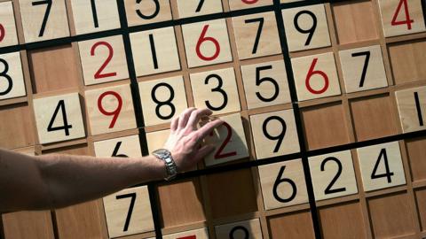 Person completing sudoku puzzle on a wooden board