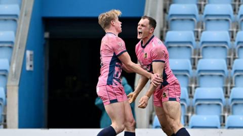 Two players in pink celebrating a try with empty stands behind them