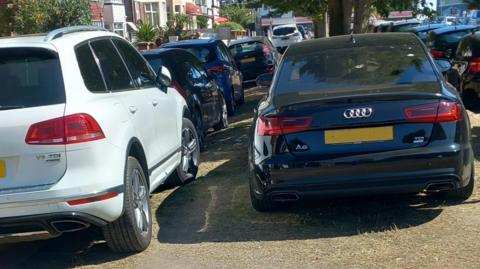 multiple cars parked on a row on a pavement in the summertime