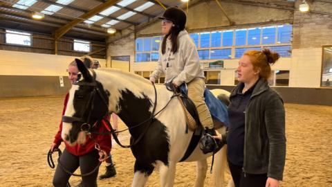 Rachel Parker rides Bernie, a black and white horse, in the arena at Middleton Park Equestrian Centre