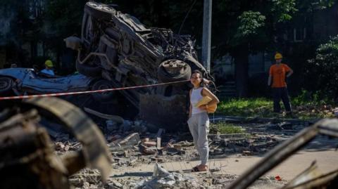 A woman looks at destroyed vehicles at the site of a damaged school which was hit during Russian drone and missile strikes