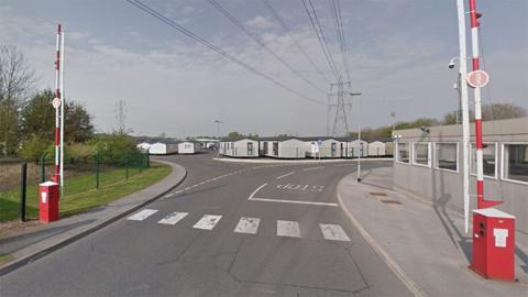 The main entrance gate of Swift caravans with red and white barriers and a number of holiday homes in the background