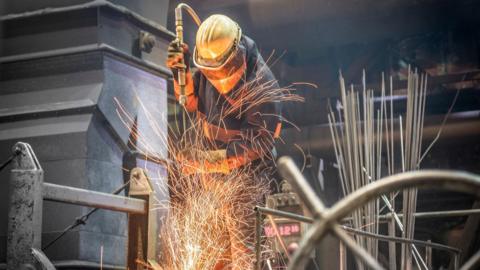 A steel worker wearing protective clothing including a mask works in a steel plant as sparks fly in the air