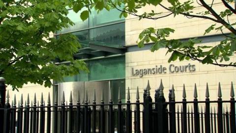 Outside of Laganside Courts, Belfast. A black wrought-iron fence stands in front of the building, which is constructed from portland stone.