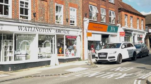 A parade of shops on a high street with red brick upper floors.