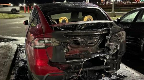 The back end of a burnt-out red car pictured at night in a parking lot