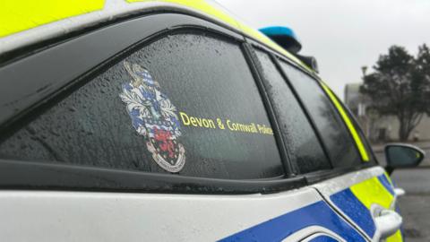 A close up view of the side of a police car. It shows a window and the Devon and Cornwall Police coat of arms.