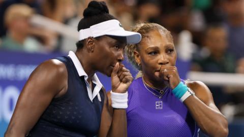 Venus and Serena Williams speak to one another during a doubles match in August