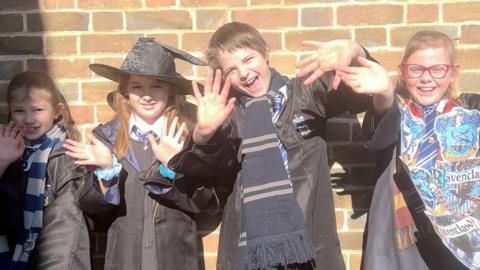 Three girls and one boy waving at the camera. They are all wearing Harry Potter-inspired costumes.