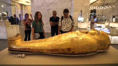 Tourists look into a glass case where a sarcophagus lies inside the Cairo Museum in Egypt.