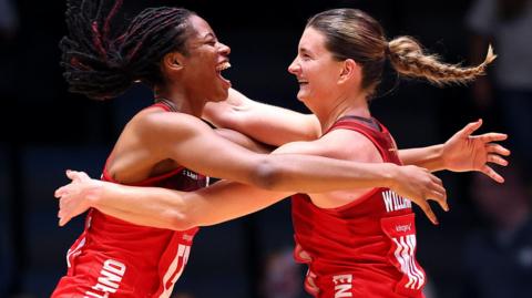 Fran Williams and Olivia Tchine, wearing England's red netball jersey, celebrate after beating South Africa to reach the semi-final by jumping in the air and hugging each other