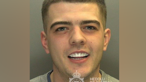 A custody photo of Coran Davies. Davies smiles looking at the camera. His white teeth are on show. 