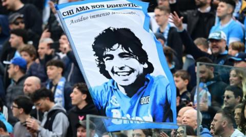 Napoli fans in the stands hold up a sign of Diego Maradona in the stands