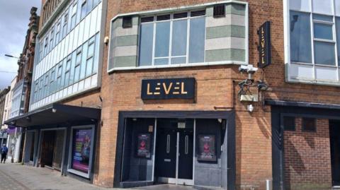 The former Level nightclub in Lincoln. It is a three storey building with grey panelling around the rows of windows. The building stands on a street corner with two black doors visible in the centre.