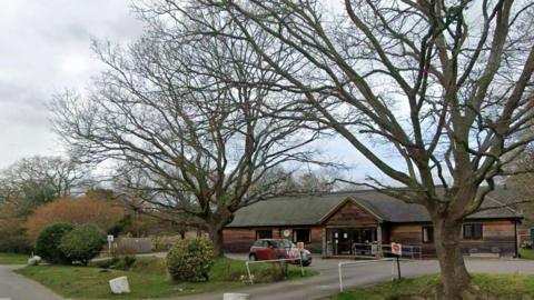 A house surrounded by bare winter trees under a grey, cloudy sky.