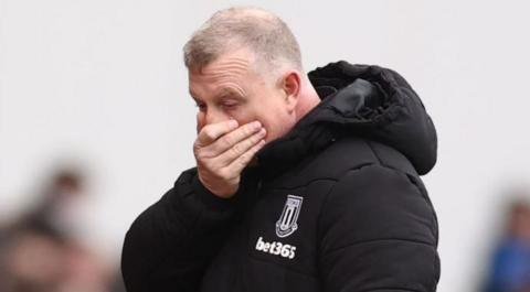 Mark Robins with his hand over his mouth in a Stoke City puffer jacket