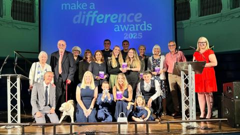 A'team' photo of the award winners on stage in front of a big screen with the words 'Make a Difference Awards 2025'