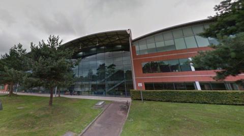 A large commercial building. There are three trees in front of it.