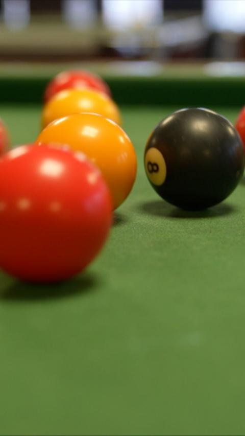 A close up of balls on a pool table. The black eight ball is on the right with two reds and two yellows to its left.