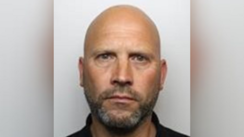 Mark Cox has grey stubble and a bald head.