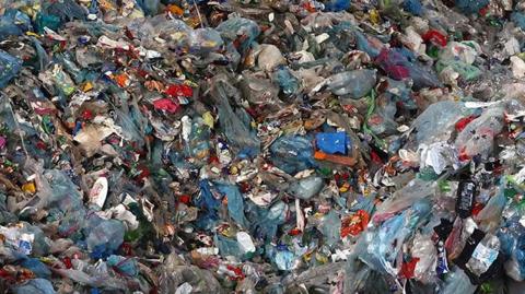 A pile of unsorted plastic recycling strewn on the ground  at sorting centre, including plastic bottles and tubs in various states