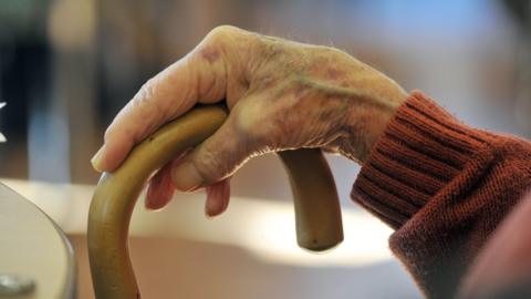 A picture of a hand holding a walking stick. The person is wearing an orange jumper