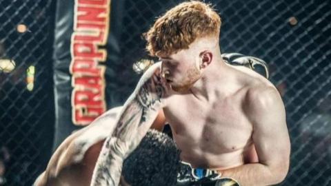 An MMA fighter with ginger hair has another MMA fighter with dark hair in a headlock in a cage