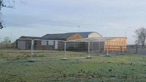 A dilapidated wood and brick building surrounded by metal fencing.