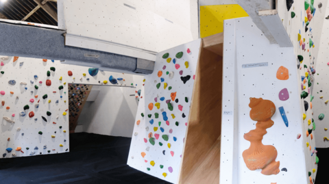 An indoor climbing wall. It has multicoloured footholds and a dark blue floor.