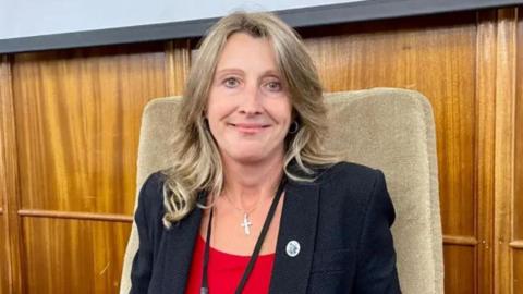 A close up shot of Spelthorne Borough Council leader Joanne Sexton looking to camera smiling wearing a dark blue jacket over a red top