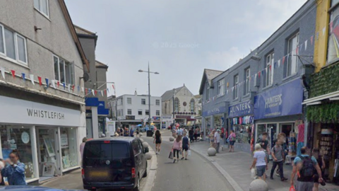 A picture taken looking down Newquay high street. There is a number of shops either side of the road.