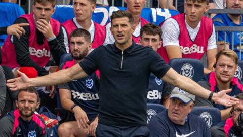John Mousinho with arms apart on the touchline