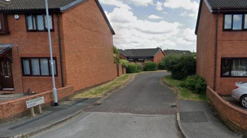 The entrance to a road of houses, with a sign at the side of the road saying Austhorpe Court