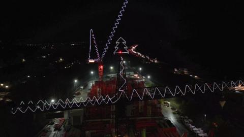 Cranes lit up with white rope lights. Atop one is a rope light Christmas tree.