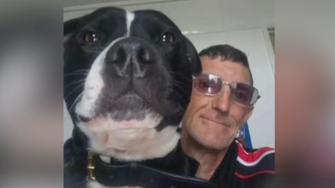 William McNicholl is pictured in a selfie-style image with his dog. William has short dark hair and dark glasses. The dog is black and white.