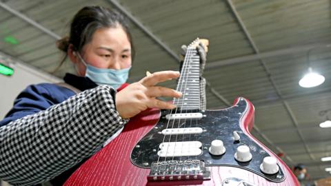An woman holds a red electric guitar as she works on the production line of musical instruments for export at a workshop in Huainan, Anhui Province of China. 