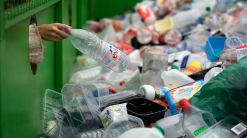 A woman depositing a plastic bottle in a recycling bin.