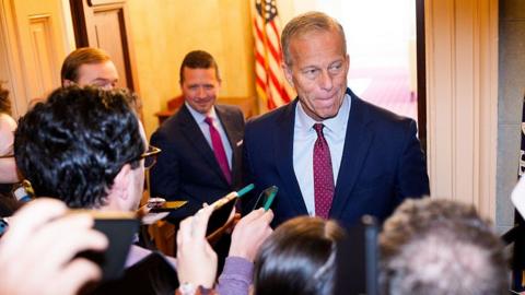 Senator John Thune speaks to reporters. He is wearing a dark-coloured suit and a red tie. 