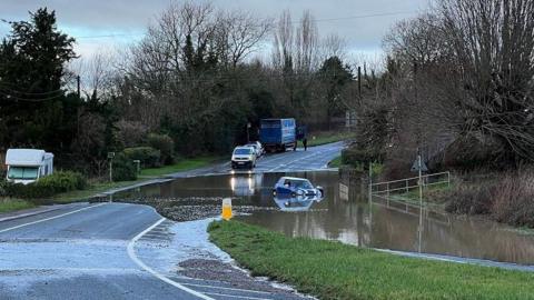 A car drives through flood water on a main road in Little Witcombe