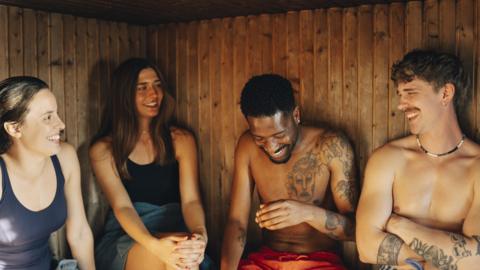 Four people laughing and smiling in a sauna.