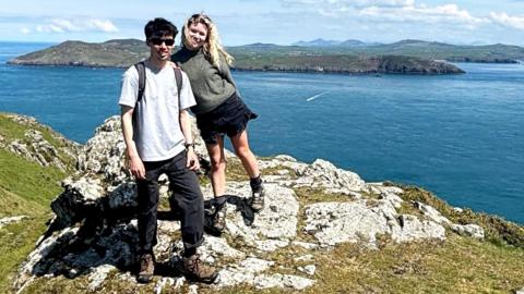 Lois and Aaron standing side by side on a hilltop overlooking the sea