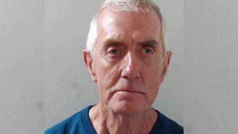 Anthony McElhone looking at the camera in a police mugshot, he has grey hair.
