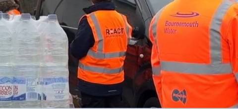 People wearing orange high vis jackets stood near bottled water outside