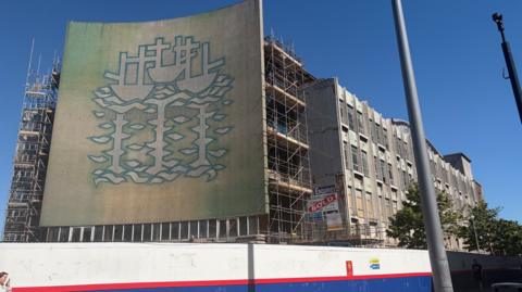 A giant mural depicting three ships covers the front of a former department store. 
