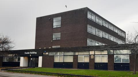 A dark brick building with glass entrance doors. The name "Forster Building" is written above the entrance in white lettering.