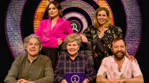 Sandi Toksvig sits in the centre. Surrounding her are Alan Davies, Joanne McNally, Sally Phillips and Andrew Maxwell