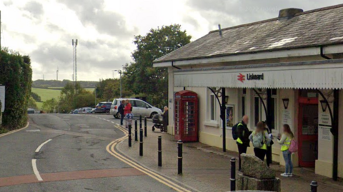 A Google Maps street view of the front of the train station in Liskeard, Cornwall. There are people stood at the entrance of the station.