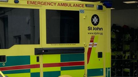 The side of a St John ambulance. It is yellow with yellow, green and red blocks.