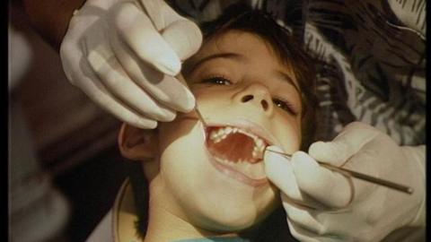 A dentist examines a child's teeth holding metal instruments in the child's mouth.